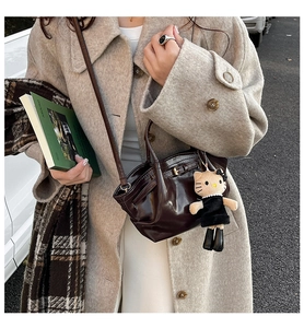 Detail of dark brown patent leather handbag with a plush charm on a beige wool coat