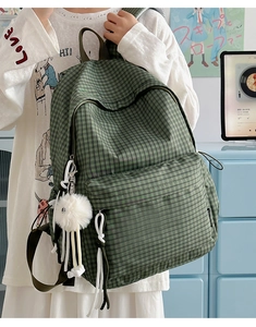 Close-up of green checkered backpack featuring a white plush pom-pom and front pocket