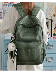 Green plaid backpack detail with plush monster charm and side pocket logo label