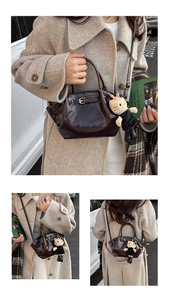 Detail of glossy chocolate brown bucket bag featuring a white plush cat charm on the handle