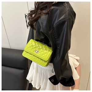 Detail of neon green quilted chain bag with gold metal clasp on model wearing black jacket