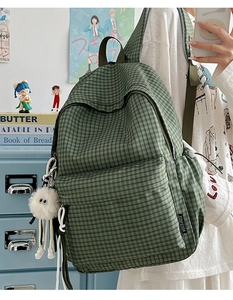 Close-up of green and white plaid canvas backpack featuring a plush monster charm detail