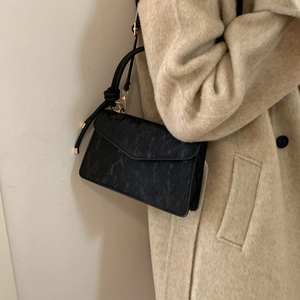 Minimalist black crossbody bag with vertical textures and gold hardware worn by model