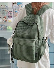 Detail of green plaid backpack featuring a plush charm and black brand label on the front