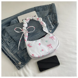 Detail of white floral shoulder bag with pink bows and ruched strap on denim backdrop