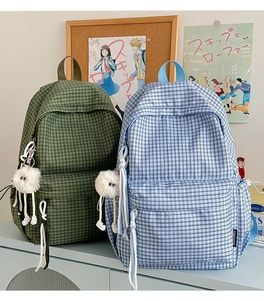 Close-up of vintage plaid backpack texture featuring a cute white plush ball keychain detail