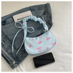 Floral blue shoulder bag with rose pattern and ruffled handle next to a book