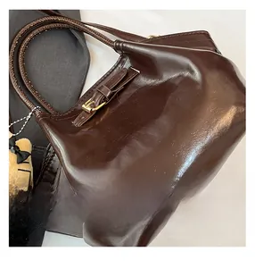 Close-up of dark brown glossy wax leather tote bag with round handle and cat pendant