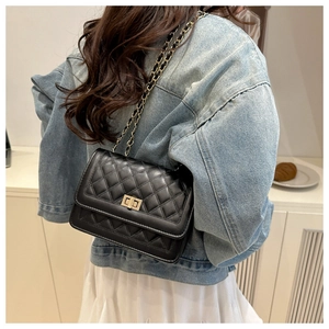 Detail view of a black quilted crossbody bag with a gold chain strap on a denim jacket