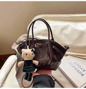 Detail of dark brown retro trapezoid handbag with decorative buckle and plush pendant