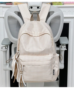 Detail of vintage plaid backpack with woven tassel charm on ergonomic white office chair