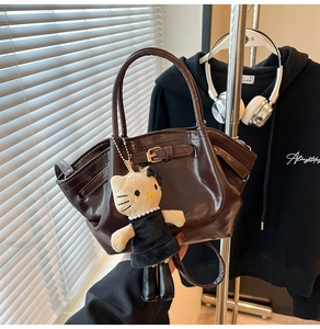 Detail of dark brown glossy patent leather bag with a cute plush character charm