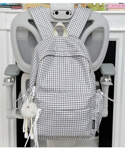 Detail of vintage plaid backpack with white zipper and plush doll pendant on a chair