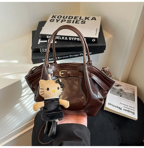 Detail of a brown glossy trapezoidal handbag featuring a cute plush doll charm and buckle
