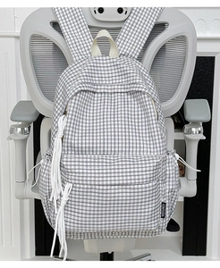 Detail of checkered backpack featuring white rope knot zippers and fabric side label