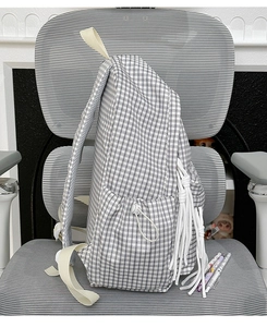 Detail of checkered backpack featuring side drawstring pockets and white tassel zipper pulls
