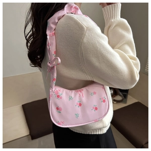 Detail of pink floral shoulder bag with bows worn over a cream cable-knit sweater