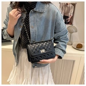 Detailed close-up of black quilted leather texture and golden metal twist-lock on the bag