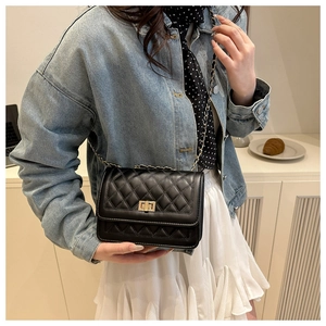 Close-up of black quilted crossbody bag with gold twist lock and chain strap on desk