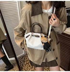 Detail of cream pleated handbag featuring dark brown handles and cute cat plush charm