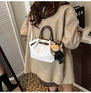 Detail of white leather handbag with brown handles and a cute plush doll charm