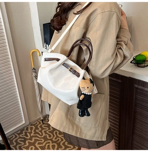 Detailed side view of white pleated bucket bag with brown straps and cute cat plush charm