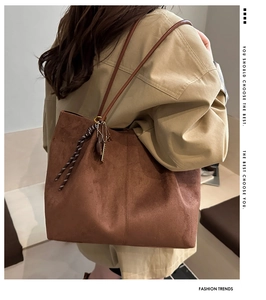 Detail of suede tote bag with leather strap and metal charm on khaki trench coat