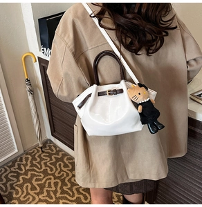 Close-up of white vintage bucket bag with brown handles and a plush cat charm detail