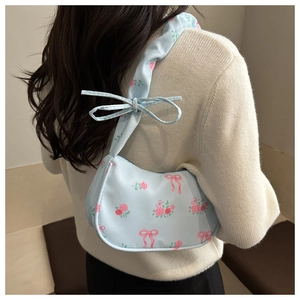 Detail of light blue shoulder bag with pink rose and bow prints worn by a model