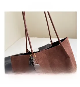 Detail of brown suede tote bag featuring a long shoulder strap and a woven pendant
