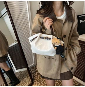 Detail of off-white tote bag featuring brown contrast handles and a plush kitty charm