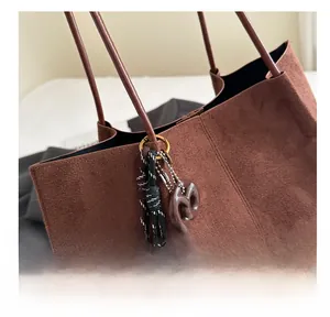 Detail view of large brown suede tote bag featuring unique woven pendant and leather handle