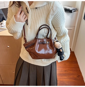 Detail of a brown glossy bucket bag with metal buckle and cute cat doll charm