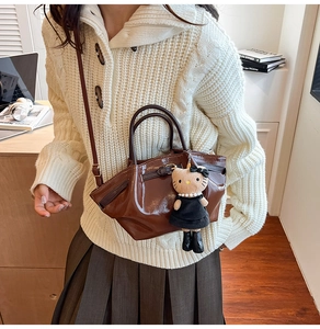 Detail of glossy brown handbag with a cute plush character charm on a white sweater