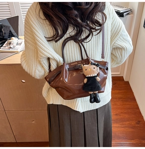 Detail of a brown glossy bucket bag with a belt buckle and cute plush charm