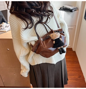 Deep brown glossy Boston bag shown as a crossbody with a cute plush charm accessory