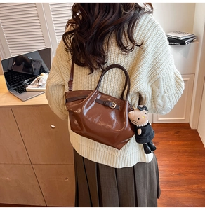 Close-up of a brown leather handbag with a vintage buckle and a cute plush kitten charm