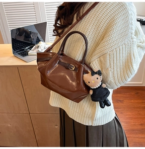 Close-up of vintage brown leather handbag featuring a cat plush charm and gold buckle