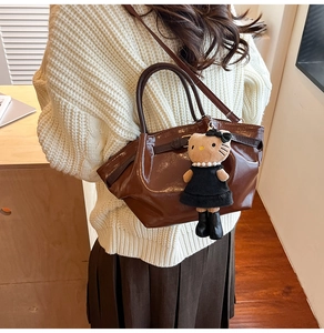 Brown patent leather tote bag with Hello Kitty charm shown on a female model shoulder