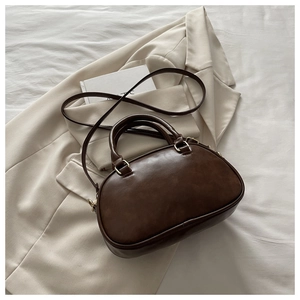 Detail of dark brown leather bowling bag with gold hardware on a beige blazer background