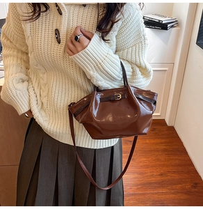Detail of a brown patent leather handbag with gold buckle, styled with a pleated skirt