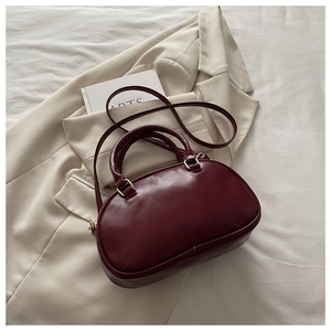 Detail of dark red leather bowling bag with gold hardware on beige blazer background