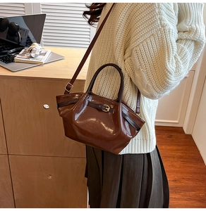 Detail of deep brown glossy handbag with vintage belt buckle and adjustable shoulder strap