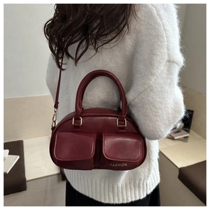 Detail of burgundy leather Boston bag with double flap pockets and gold logo on white knitwear