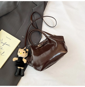 Detail of glossy dark brown pleated handbag with a cat doll charm on a gray blazer
