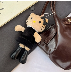 Close-up of plush cat pendant in black velvet dress with pearl necklace on a handbag