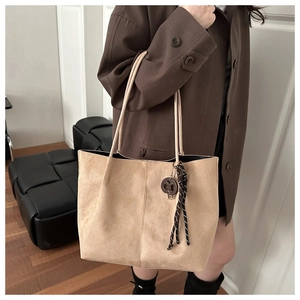 Detail of beige suede tote bag showing soft texture and woven pendant decoration