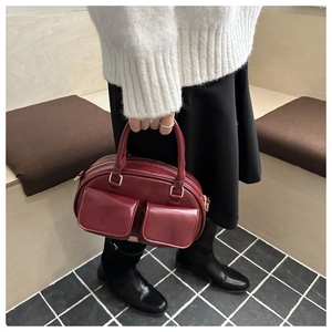 Detail of burgundy leather Boston bag featuring dual front flap pockets and golden zippers