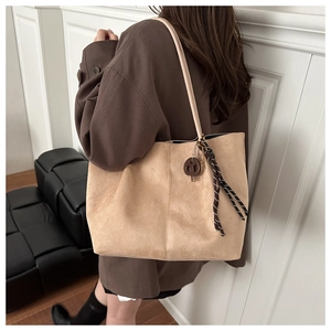 Détail du sac cabas en daim kaki clair montrant la texture mate et le pendentif décoratif