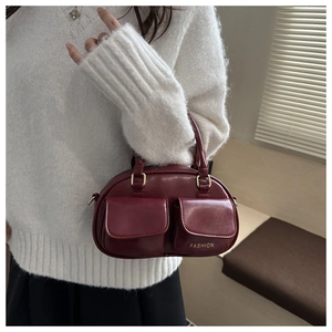 Detail of dark red bowling bag featuring dual front flap pockets and gold fashion text